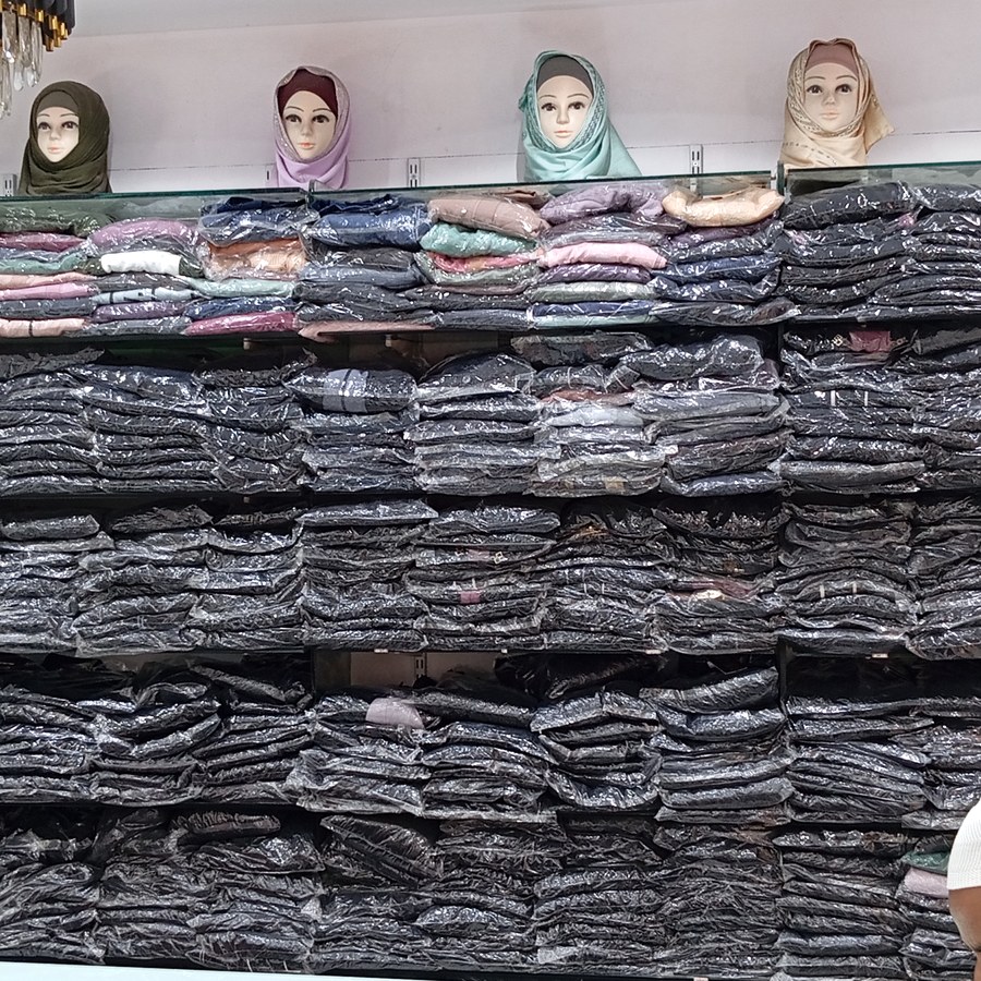 Wall of shelved, packaged burqas beneath a row of hijab-draped mannequin heads