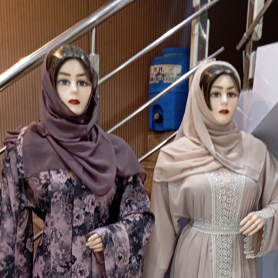 Two mannequins dressed in patterned and plain abayas with hijabs